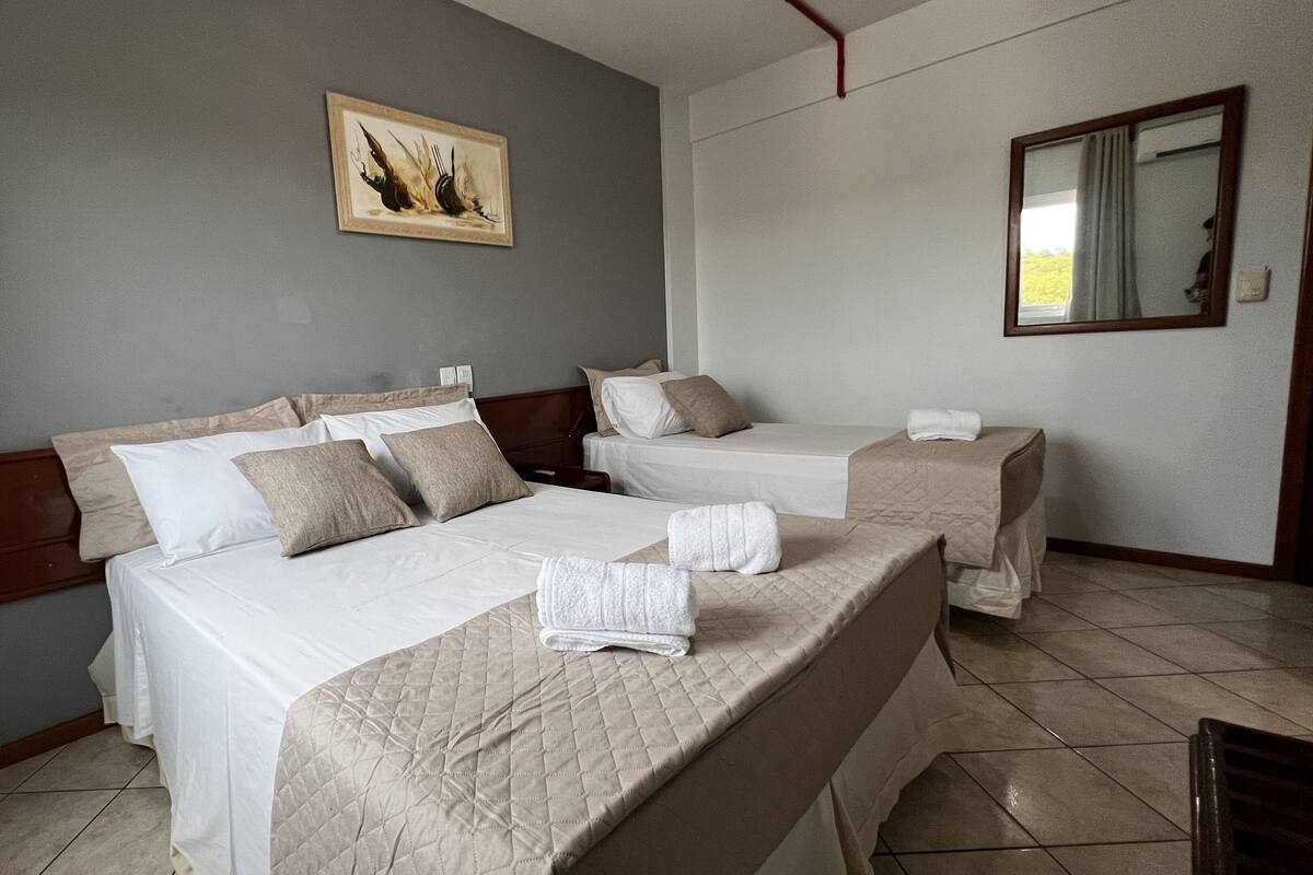A hotel room with two beds, a painting on the wall, and a mirror.