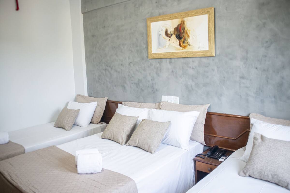A hotel room with two single beds, a double bed, a bedside table with a phone, and a painting on the wall.