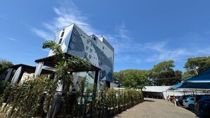 Um edifício moderno com um design geométrico único, rodeado por vegetação e um céu claro.