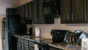 A modern kitchen with dark cabinetry, a stainless steel refrigerator, a microwave, and a stove.