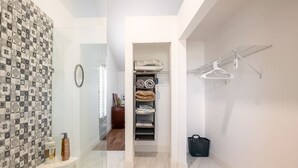 A modern bathroom with a tiled backsplash, a glass shower enclosure, a white vanity with a mirror, and a laundry area with a drying rack and basket. - Private Pool Home near 5th Ave, Old Naples and Beach (Naples)