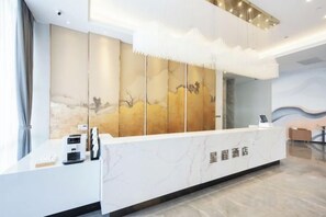 Un comptoir d’accueil au design moderne, un grand panneau décoratif et une vue dégagée sur le hall d’entrée.