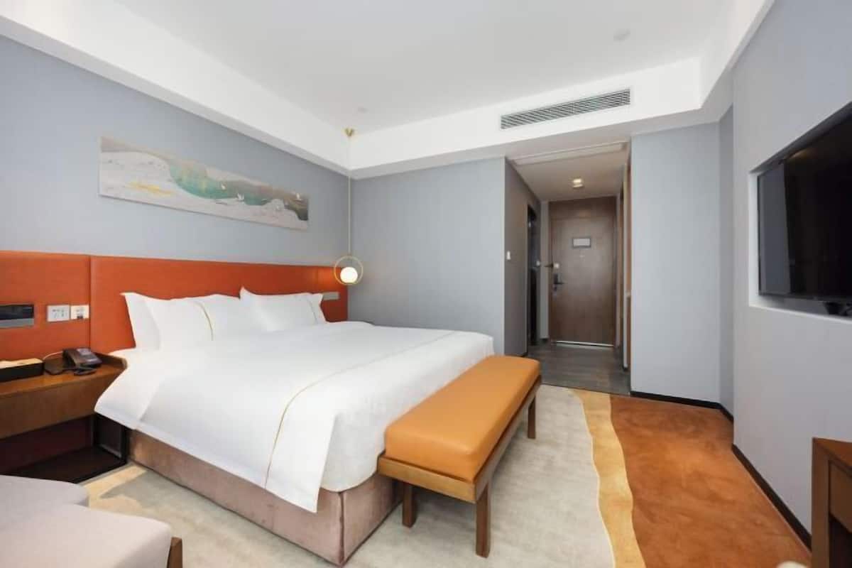 A hotel room with a bed, a bench, a nightstand, a TV, and a painting on the wall.