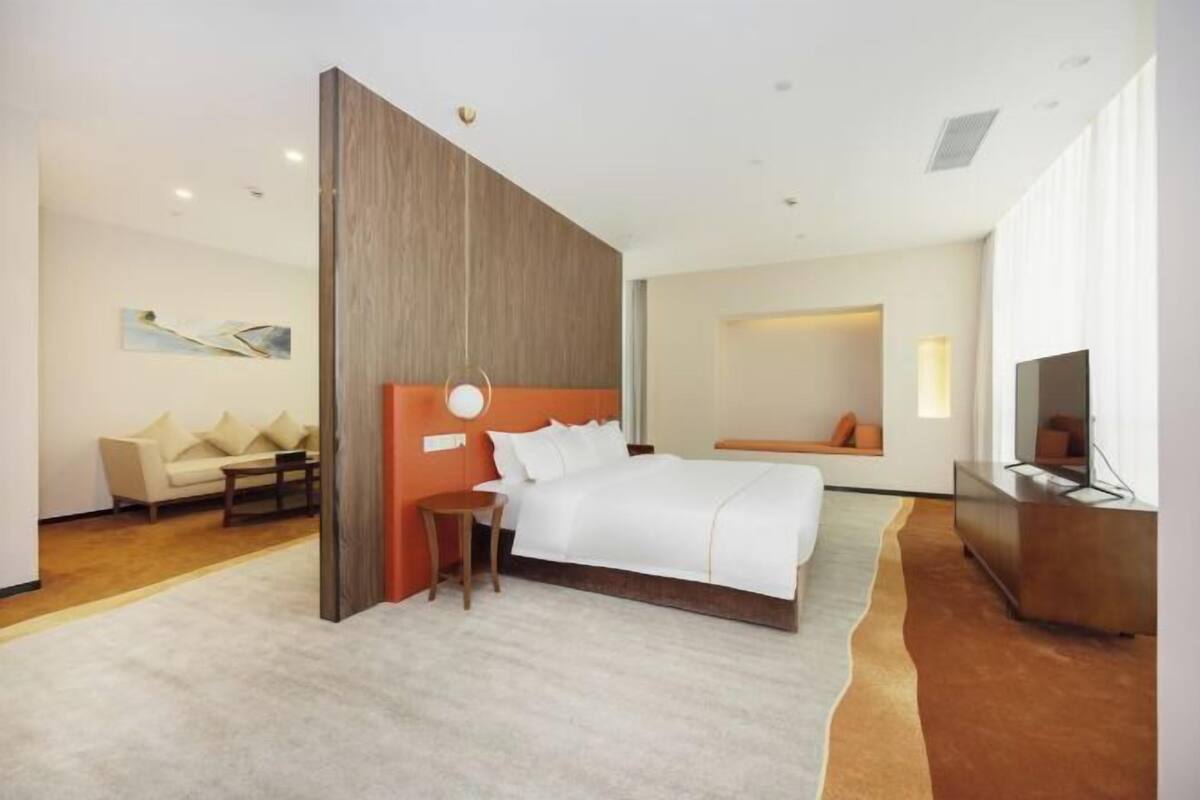 A modern hotel room with a large bed, a seating area with a sofa and armchairs, a TV, and a small table.