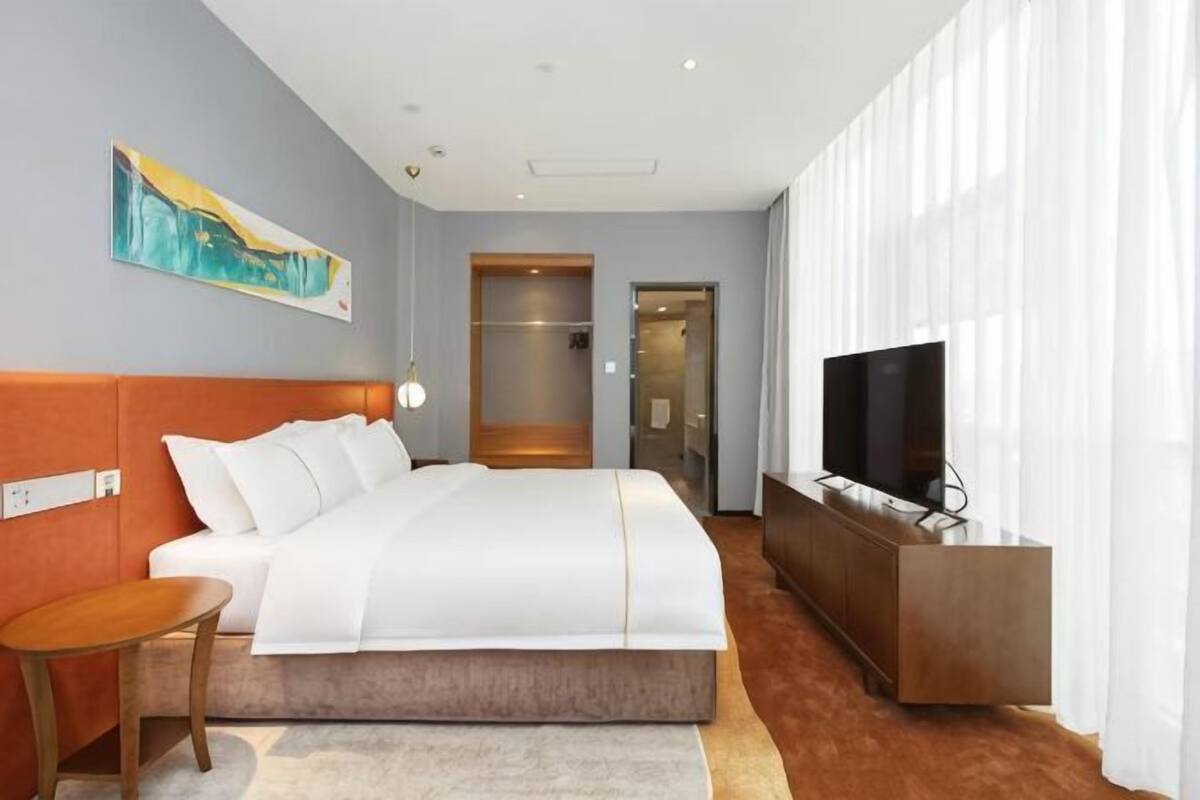 A hotel room with a bed, a TV, a desk, and a painting on the wall.
