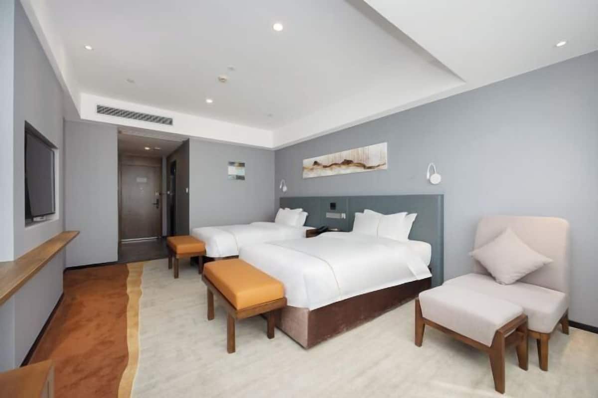 A modern hotel room with a large bed, a sofa, a chair, and a TV.