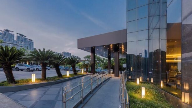 A modern hotel entrance with a glass facade, outdoor seating area, and palm trees. - Motel (Shanghai Lujiazui Yushan Road Yuanshen Sports Center) (Shanghai)