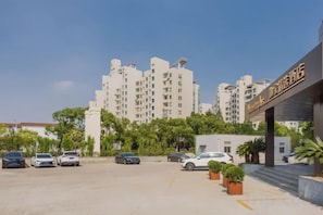 Un parking avec plusieurs voitures, un bâtiment avec une enseigne et, au fond, un immeuble de grande hauteur.
