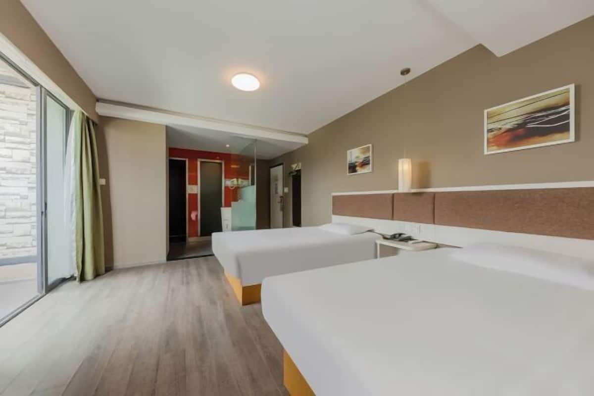 A hotel room with two beds, a large window, a door leading to a corridor, and a painting on the wall.