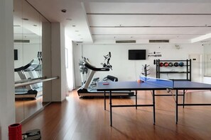 Une salle de sport équipée de matériel d’exercice, d’une table de ping-pong et d’un téléviseur fixé au mur.