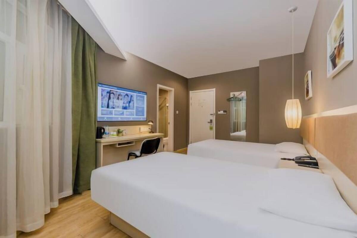A hotel room with two beds, a desk with a computer, a chair, and a shower area.