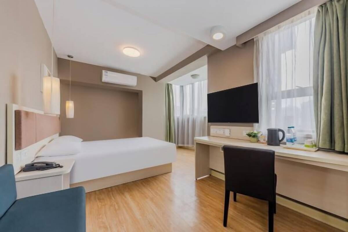 A hotel room with a bed, a desk, a chair, a TV, and a window with curtains.