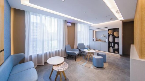 A modern living room with a sofa, two chairs, a coffee table, and a small side table. There is a large window with sheer curtains, a ceiling light, and a built-in shelf with decorative items. - Homeinn·NEO(Shenyang Tiexi Square Glide Shengjing Hospital Xinghua Metro Station) (Shenyang)