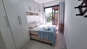 A bedroom with a bed, a wardrobe, a small stool, and a view of the outside. - Apto moderno com miniquintal e piscina (Rio de Janeiro)
