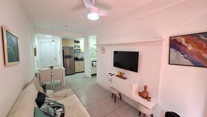 A modern living room with a sofa, TV, and a dining area with a table and chairs. - Apto moderno com miniquintal e piscina (Rio de Janeiro)