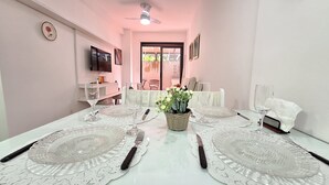 A dining table set with clear glass plates, silverware, and a centerpiece of white flowers. - Apto moderno com miniquintal e piscina (Rio de Janeiro)