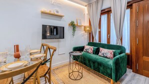 A living room with a green sofa, a dining table with chairs, a TV mounted on the wall, and a wooden cabinet. - Francos Cathedral Terrace Apartment (Sevilla)