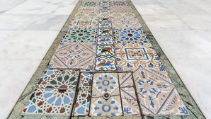 A courtyard with a tiled floor leading to a building entrance, featuring a column and a decorative tile border. - Francos Cathedral Terrace Apartment (Sevilla)