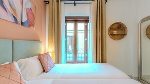 A hotel room with a bed, a headboard, a window with curtains, and a wall-mounted shelf. - Francos Cathedral Terrace Apartment (Sevilla)