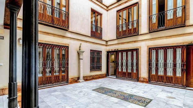 A spacious courtyard with marble flooring, wooden balconies, and barred windows. - Francos Cathedral Terrace Apartment (Sevilla)