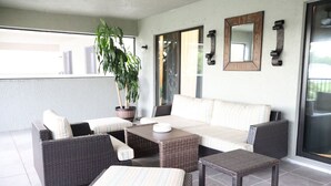 Un espacio de patio cubierto con mobiliario de mimbre, una planta en maceta y un ventanal corredero.