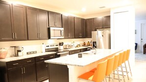 Una cocina moderna con gabinetes oscuros, electrodomésticos de acero inoxidable y una isla central con taburetes.