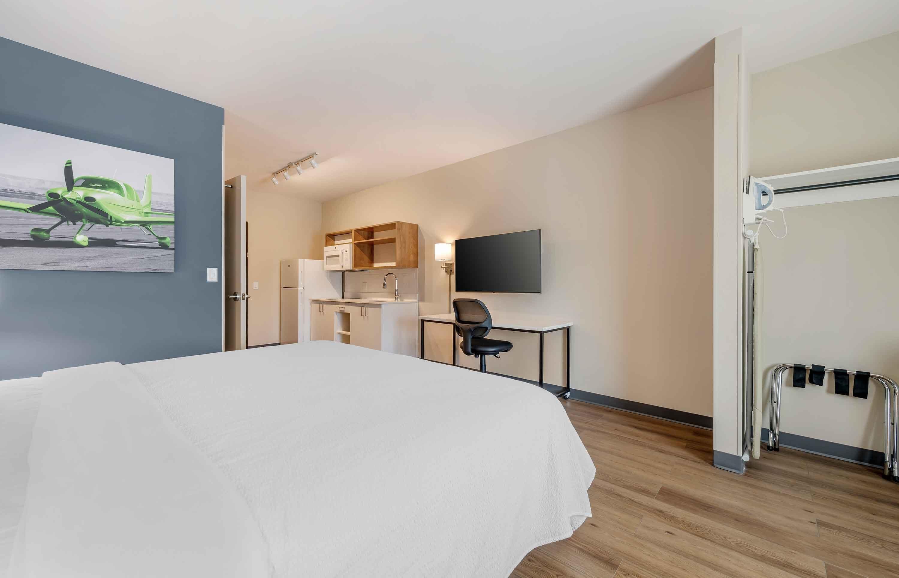 Une chambre d’hôtel comprenant un lit, un bureau avec une chaise, une télévision, un four à micro-ondes et une petite kitchenette.