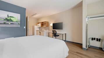 Une chambre d’hôtel comprenant un lit, un bureau avec une chaise, une télévision, un four à micro-ondes et une petite kitchenette.