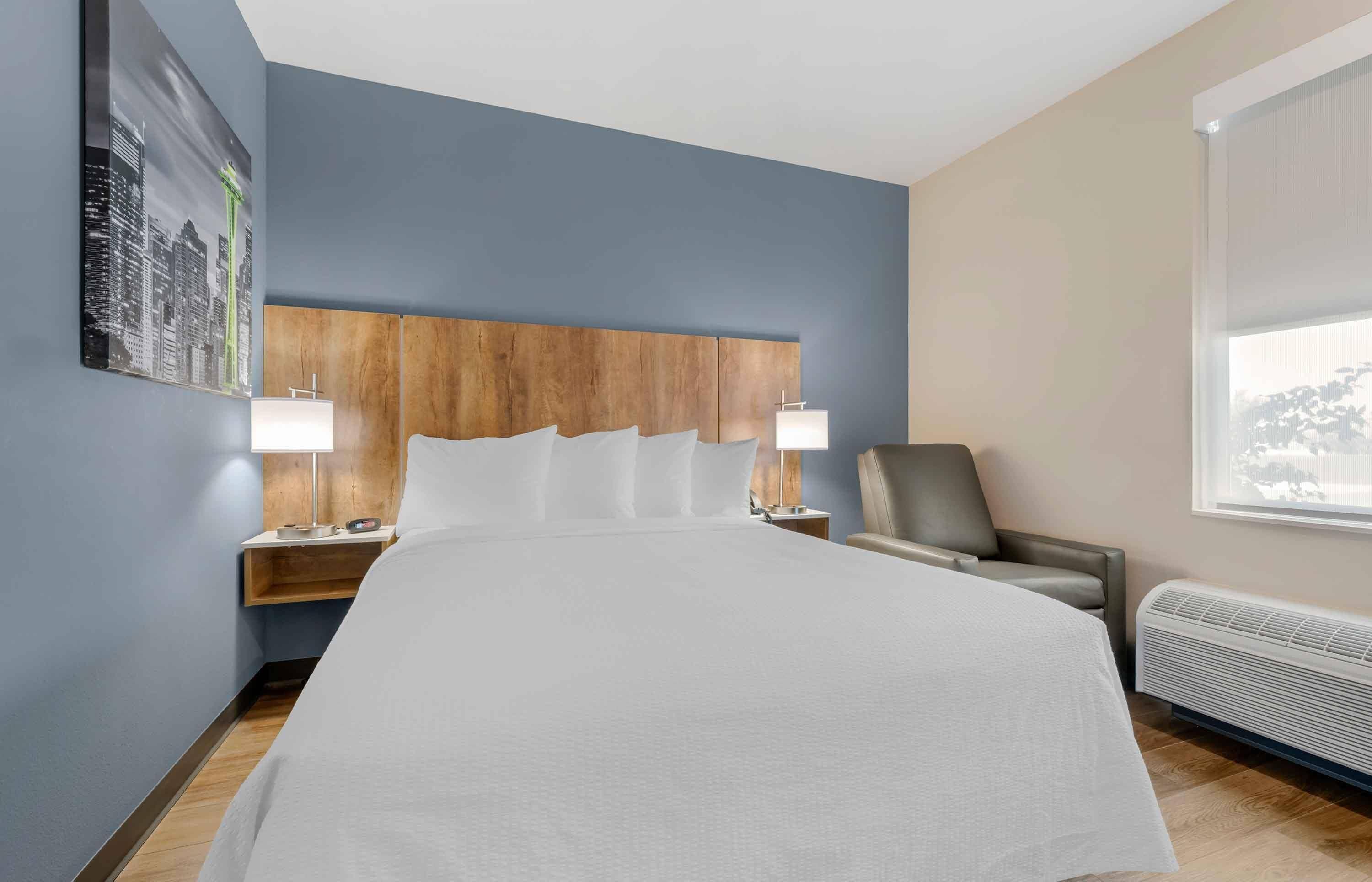 Habitación de hotel con una cama grande, dos mesitas de noche con lámparas, una silla, una ventana y un calentador de pared.