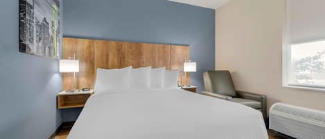 A hotel room with a large bed, two bedside tables with lamps, a chair, a window, and a wall-mounted heater.