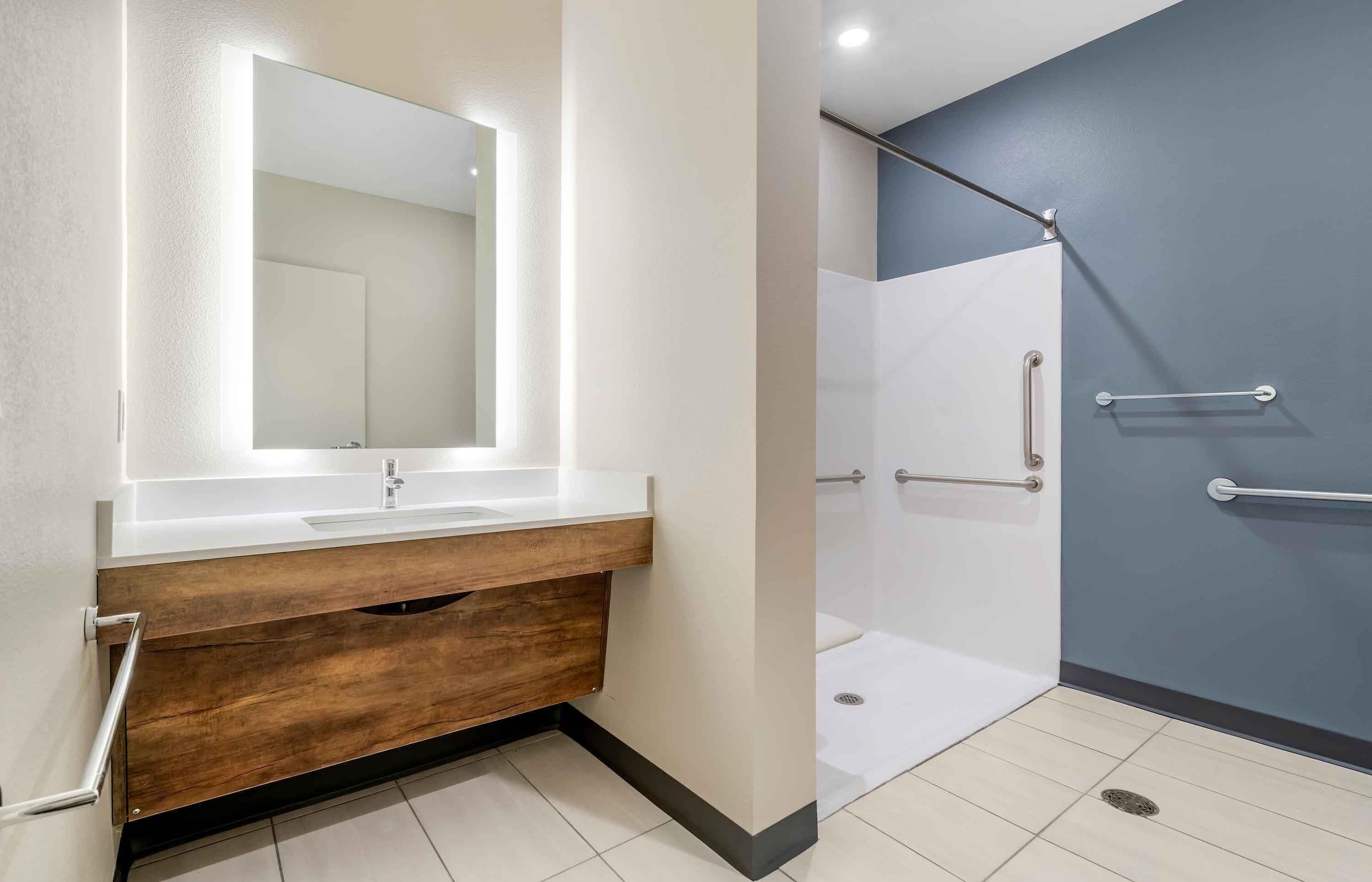 A modern bathroom with a white vanity, a large mirror, and a shower area with grab bars.