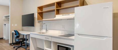 Una cocina compacta con un refrigerador blanco, un microondas, un lavamanos y una estantería de madera.