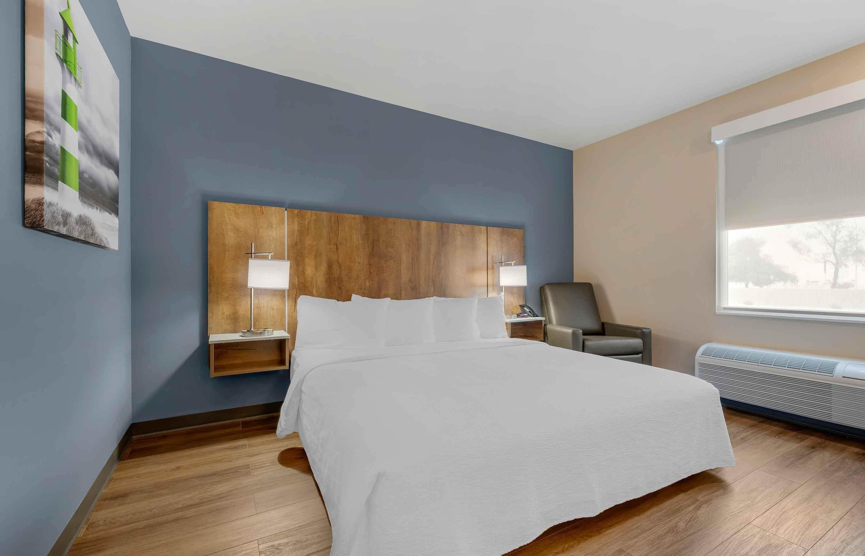 A hotel room with a large bed, wooden headboard, two bedside tables with lamps, a chair, and a window with a view.