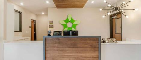 A reception area with a wooden reception desk, a green abstract wall art, and a modern light fixture.