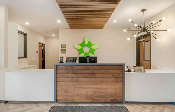 A reception area with a wooden reception desk, a green abstract wall art, and a modern light fixture. - Extended Stay America Premier Suites – Phoenix - Chandler – Airport (Chandler)