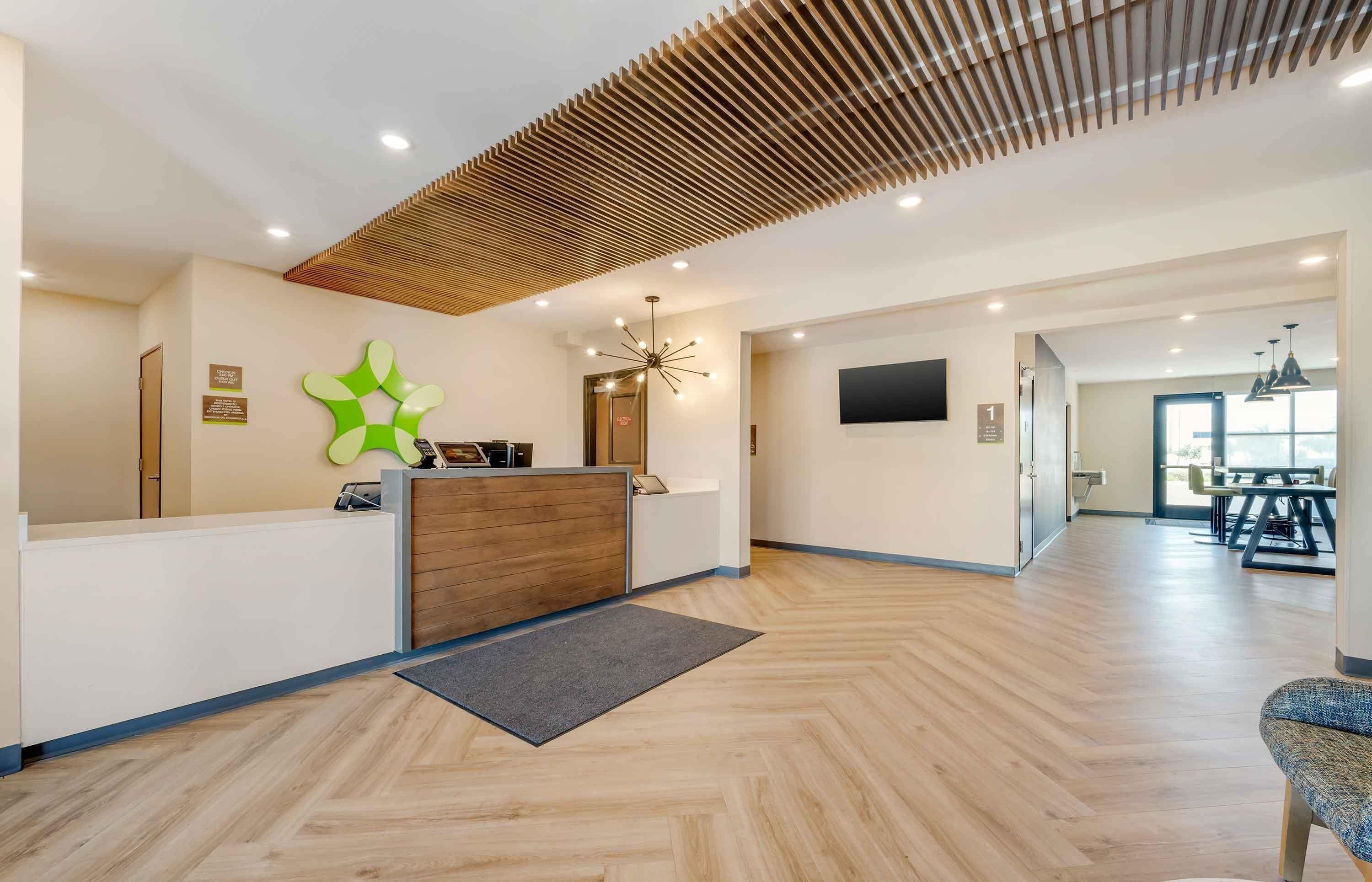 A reception area with a wooden reception desk, a green abstract wall decoration, and a modern ceiling design.