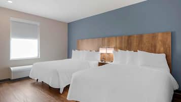 A hotel room with two beds, a wooden headboard, a bedside table with a lamp, and a large window providing natural light.