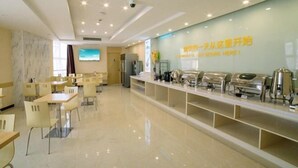 A modern dining area with tables and chairs, a buffet counter with food service equipment, and a wall with text. - Yingdong Motel (Shanghai)