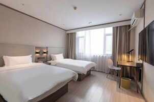 A hotel room with two beds, a desk, a chair, a TV, and a large window with curtains.
