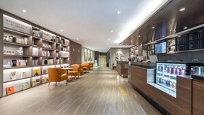 A modern hotel lobby with a long reception desk, seating area, and bookshelves. - HanTing Hotel (Qinhuangdao Development Zone Yanshan University) (Qinhuangdao)