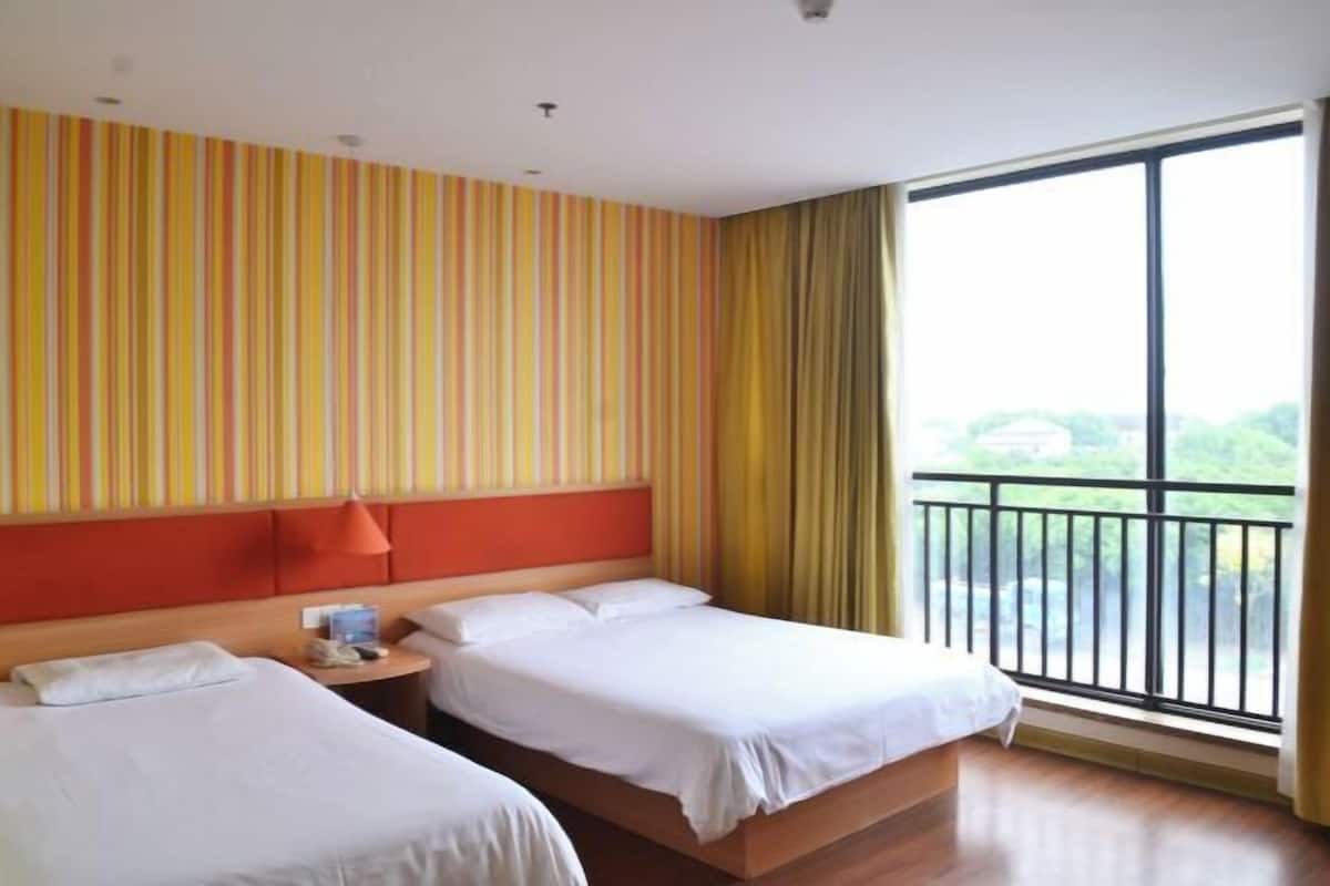 Ein Hotelzimmer mit zwei Betten, einem großen Fenster und einem Balkon, sowie einer gestreiften Wand.