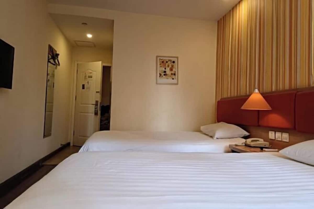 Ein Hotelzimmer mit zwei Betten, einer Nachttischlampe, einem Telefon und einem gerahmten Bild an der Wand.
