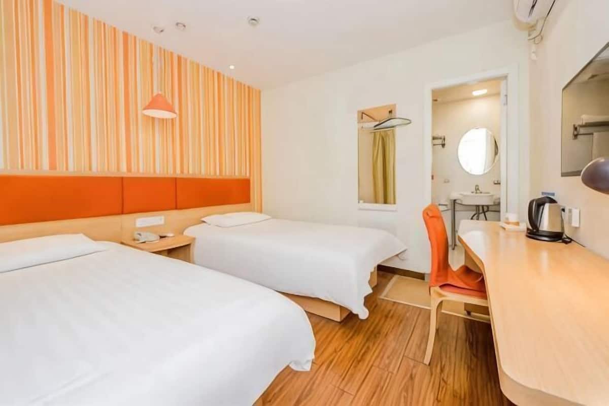 Ein Hotelzimmer mit zwei Betten, einem Holztisch, einem Stuhl, einem Spiegel und einem Fenster.