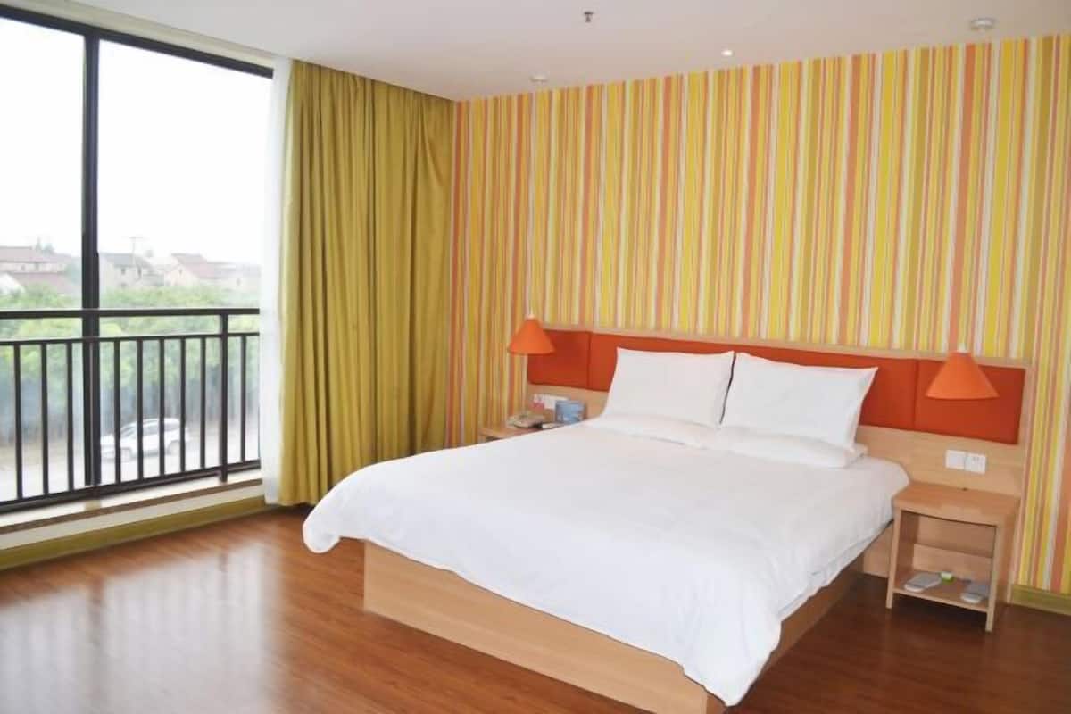Ein Hotelzimmer mit einem großen Bett, einem Nachttisch, einem Fenster mit Vorhängen und einer gestreiften Wand.