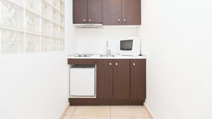 Een kleine keuken met donkerhouten kastjes, een witte koelkast, een magnetron en een spoelbak.