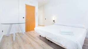 Een slaapkamer met een houten deur, een glazen tafel, een bed met wit beddengoed en een wandlamp.