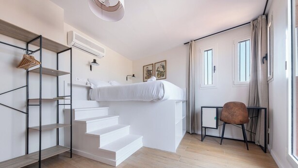 Ein modernes Schlafzimmer mit einer eingebauten Bettenkonstruktion, weißen Wänden, Holzboden, einer Treppe mit Metallrahmen und einem kleinen Tisch mit Stuhl.