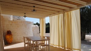An outdoor patio with a wooden table and chairs, a large vase, and a view of the surrounding landscape. - Trullo Sogni Di Pietra - Ostuni (Ostuni)