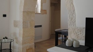 A room with a stone wall, a white table with a lamp, and a chair. - Trullo Sogni Di Pietra - Ostuni (Ostuni)