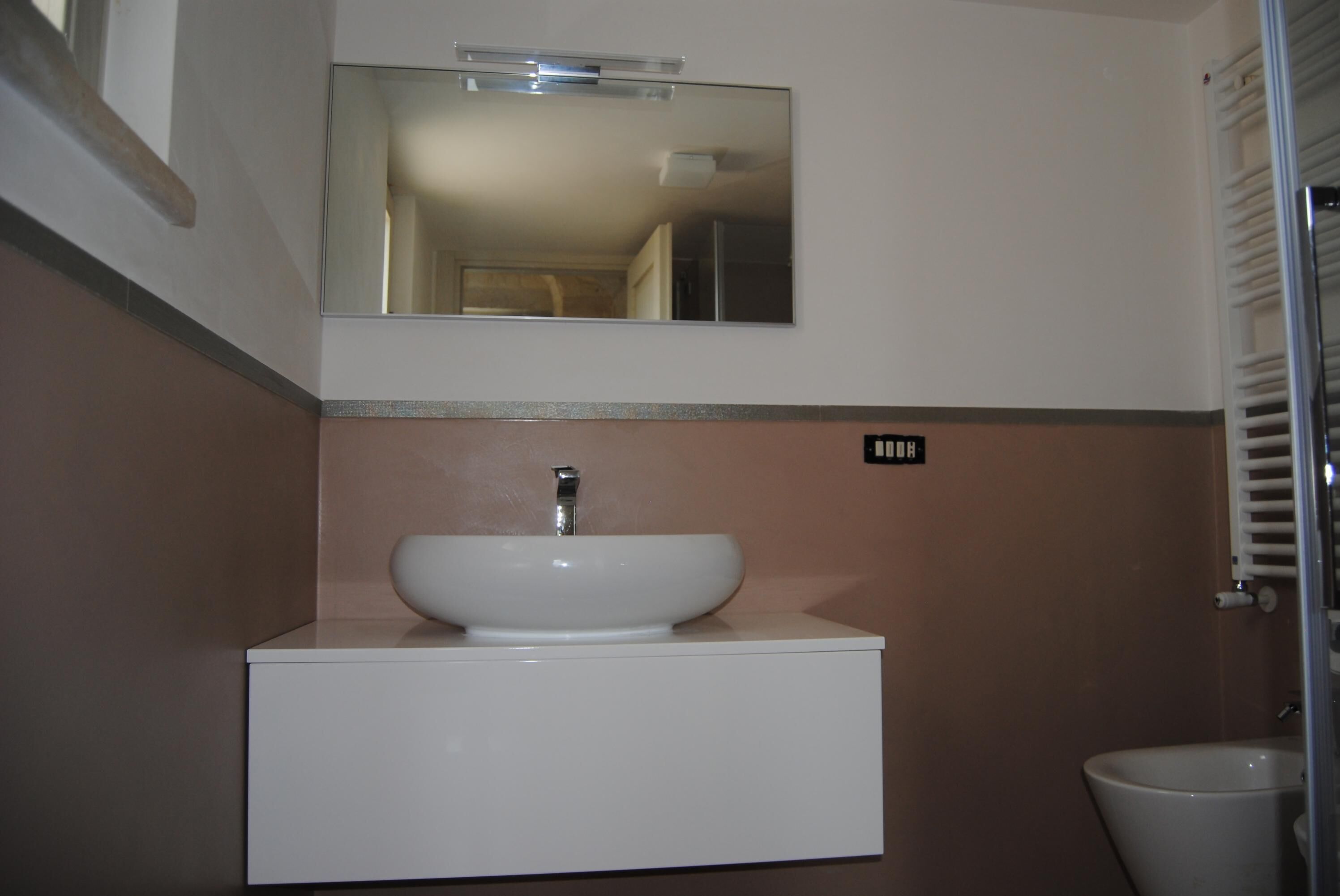 Une salle de bain avec un lavabo blanc, un miroir au-dessus et des toilettes sur la droite.